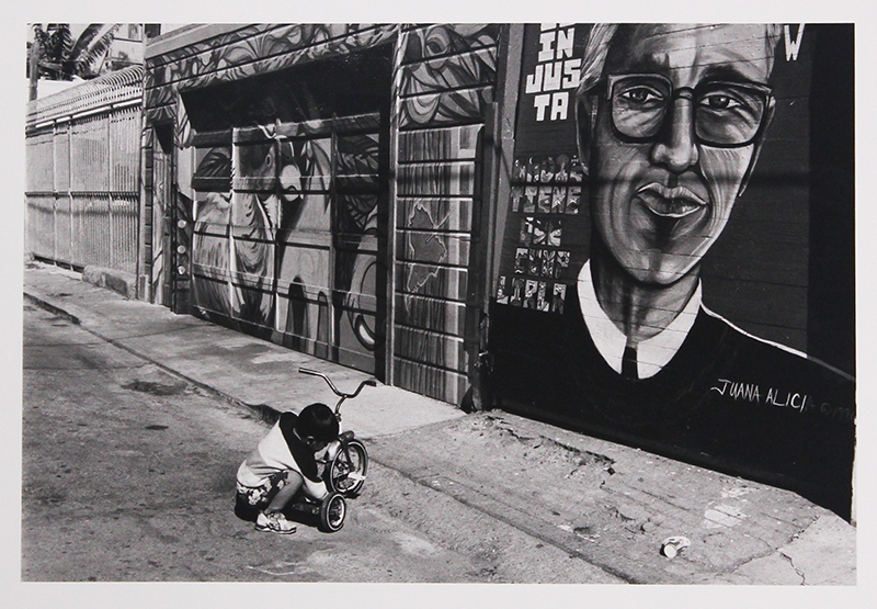 Untitled (Boy with tricycle, on street with murals) by Unidentified